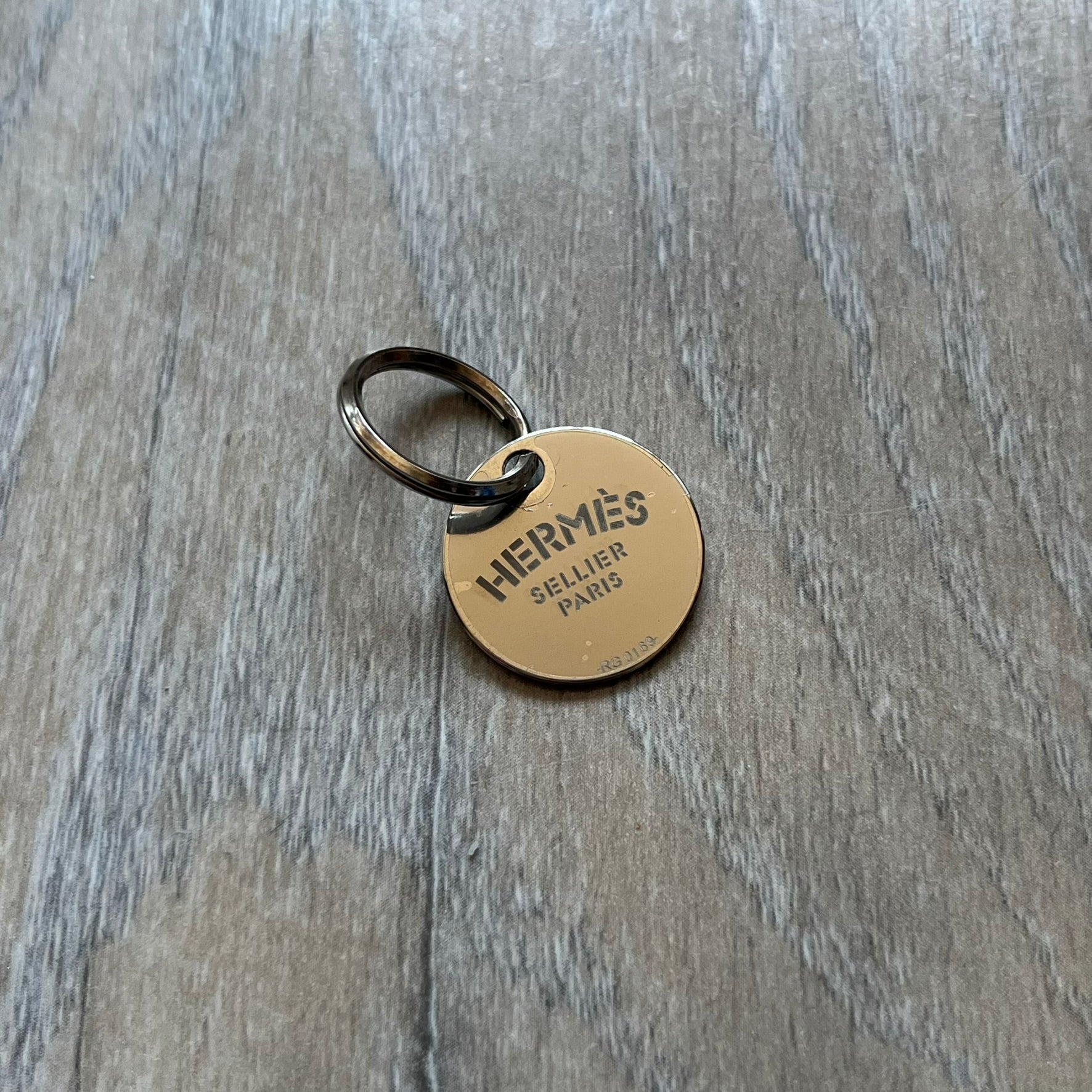 Small model Hermès Étrivière dog collar crafted from Natural Sable bridle leather. The collar features a stirrup-shaped buckle stamped HERMÈS, a metal D-ring for leash attachment, and leather stamped “HERMÈS PARIS MADE IN FRANCE.” It includes a 2 cm silver-plated stainless steel medal engraved “Hermès Sellier Paris,” with the reverse side suitable for engraving