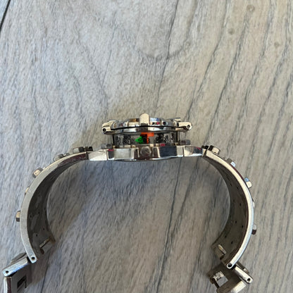Hi-Tek Alexander 90's Side View Latch Analog Watch is a Hi-Tek Alexander watch with a rigid metal bracelet made of two sections featuring a raised circular pattern. The watch case has a latch-style cover that can be closed over the dial and is fully metallic. The dial is black and replaces traditional numbers with Hi-Tek figures - seconds hand is also a figure, while the hour and minute indicators are colored green and orange. The sides of the case are made of glass, allowing the time to be viewed from mult