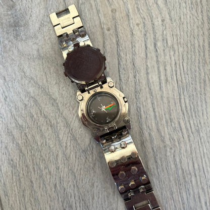 Hi-Tek Alexander 90's Side View Latch Analog Watch is a Hi-Tek Alexander watch with a rigid metal bracelet made of two sections featuring a raised circular pattern. The watch case has a latch-style cover that can be closed over the dial and is fully metallic. The dial is black and replaces traditional numbers with Hi-Tek figures - seconds hand is also a figure, while the hour and minute indicators are colored green and orange. The sides of the case are made of glass, allowing the time to be viewed from mult