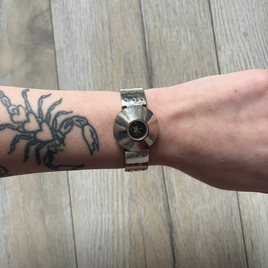 Hi-Tek Alexander “Cylinder” 90’s Analog Watch is a 1990s English-made timepiece featuring a black dial with a small Hi-Tek logo as the seconds hand. The cylindrical 3D case rises from the wrist, making the dial visible only from above, and the straps feature raised dot detailing. The stainless steel case back is branded with the Hi-Tek logo, designed specifically for smaller wrists.