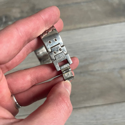 Hi-Tek Alexander “Cylinder” 90’s Analog Watch is a 1990s English-made timepiece featuring a black dial with a small Hi-Tek logo as the seconds hand. The cylindrical 3D case rises from the wrist, making the dial visible only from above, and the straps feature raised dot detailing. The stainless steel case back is branded with the Hi-Tek logo, designed specifically for smaller wrists.