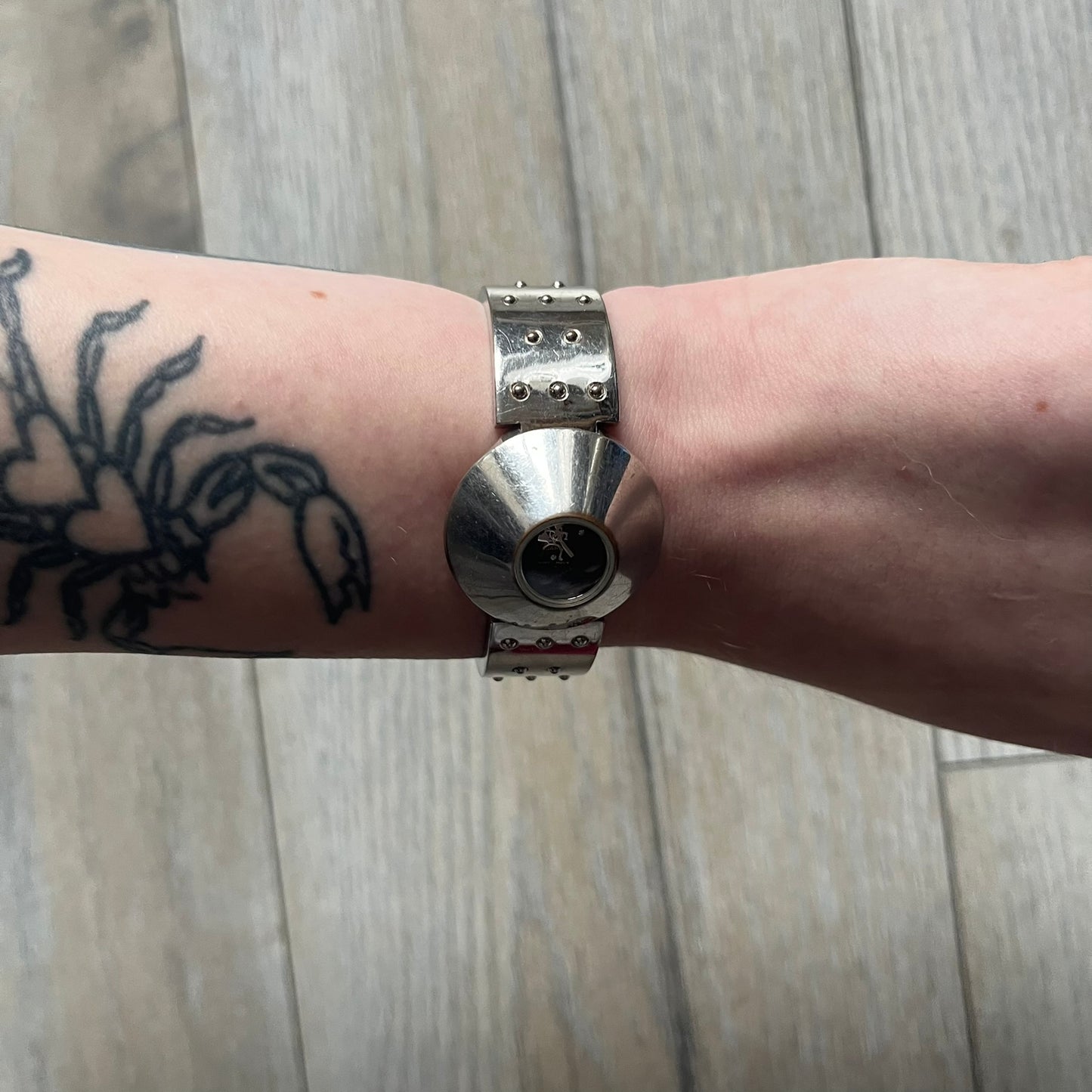 Hi-Tek Alexander “Cylinder” 90’s Analog Watch is a 1990s English-made timepiece featuring a black dial with a small Hi-Tek logo as the seconds hand. The cylindrical 3D case rises from the wrist, making the dial visible only from above, and the straps feature raised dot detailing. The stainless steel case back is branded with the Hi-Tek logo, designed specifically for smaller wrists.