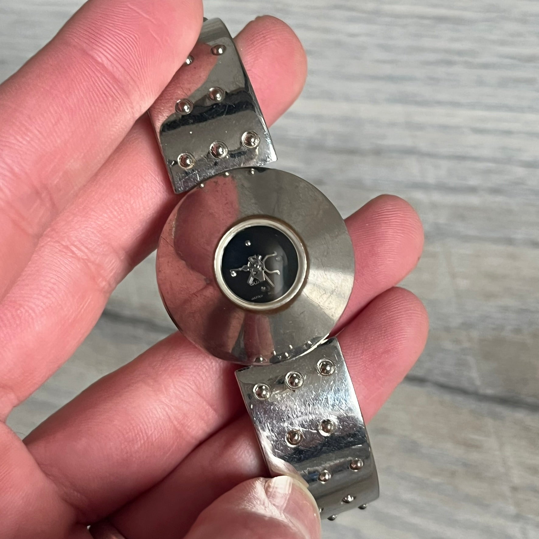 Hi-Tek Alexander “Cylinder” 90’s Analog Watch is a 1990s English-made timepiece featuring a black dial with a small Hi-Tek logo as the seconds hand. The cylindrical 3D case rises from the wrist, making the dial visible only from above, and the straps feature raised dot detailing. The stainless steel case back is branded with the Hi-Tek logo, designed specifically for smaller wrists.