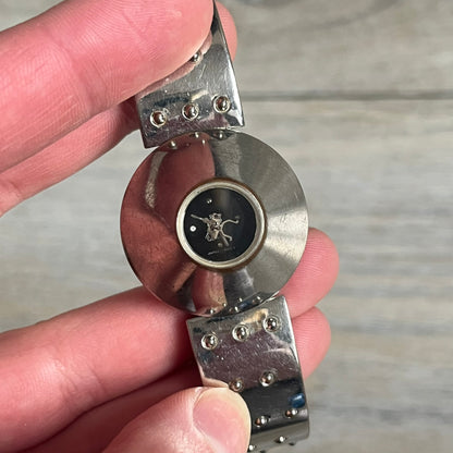 Hi-Tek Alexander “Cylinder” 90’s Analog Watch is a 1990s English-made timepiece featuring a black dial with a small Hi-Tek logo as the seconds hand. The cylindrical 3D case rises from the wrist, making the dial visible only from above, and the straps feature raised dot detailing. The stainless steel case back is branded with the Hi-Tek logo, designed specifically for smaller wrists.