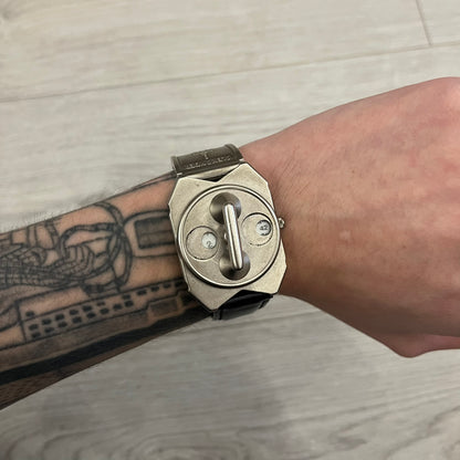 Hi-Tek Alexander “Jump Hour” 90's Analog Watch with a rare octagonal steel case and innovative rotation disc display. Hours appear in the left window and minutes in the right, revealed by the unique turnable cover. Made in England, this vintage 1990s watch features a chrome-plated stainless steel case, genuine leather strap, and an original design by Alexander Tasou of Hi-Tek Designs London. A true collector’s piece that is no longer in production.