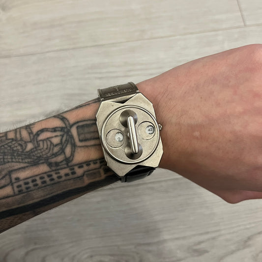 Hi-Tek Alexander “Jump Hour” 90's Analog Watch with a rare octagonal steel case and innovative rotation disc display. Hours appear in the left window and minutes in the right, revealed by the unique turnable cover. Made in England, this vintage 1990s watch features a chrome-plated stainless steel case, genuine leather strap, and an original design by Alexander Tasou of Hi-Tek Designs London. A true collector’s piece that is no longer in production.