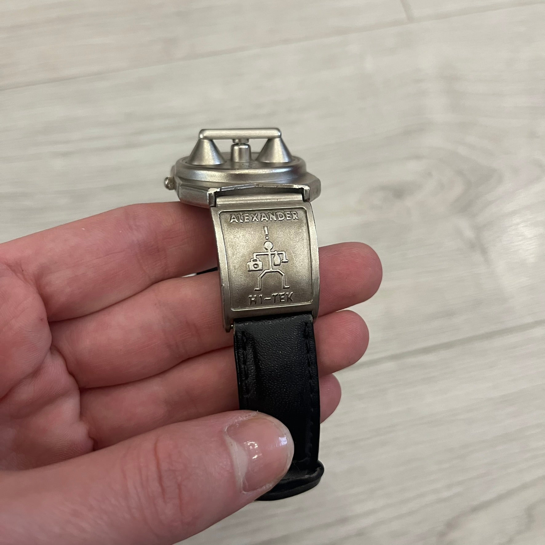 Hi-Tek Alexander “Jump Hour” 90's Analog Watch with a rare octagonal steel case and innovative rotation disc display. Hours appear in the left window and minutes in the right, revealed by the unique turnable cover. Made in England, this vintage 1990s watch features a chrome-plated stainless steel case, genuine leather strap, and an original design by Alexander Tasou of Hi-Tek Designs London. A true collector’s piece that is no longer in production.