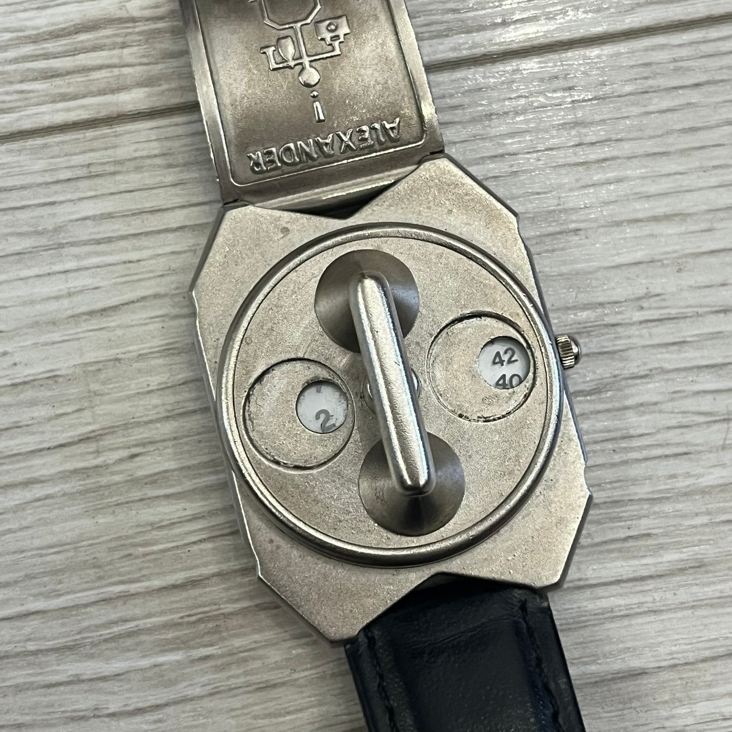 Hi-Tek Alexander “Jump Hour” 90's Analog Watch with a rare octagonal steel case and innovative rotation disc display. Hours appear in the left window and minutes in the right, revealed by the unique turnable cover. Made in England, this vintage 1990s watch features a chrome-plated stainless steel case, genuine leather strap, and an original design by Alexander Tasou of Hi-Tek Designs London. A true collector’s piece that is no longer in production.