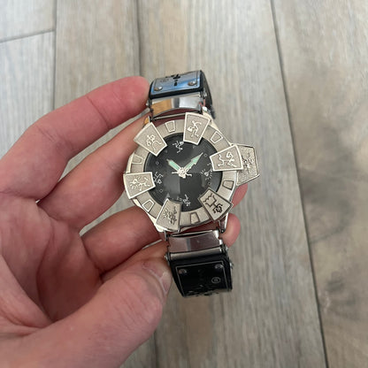 Hi-Tek Alexander “Running Man” 1990s Analog Watch is a stainless steel watch featuring a black dial and full steel case with integrated bracelet strap. The bezel includes a rotating top layer decorated with Hi-Tek character figures in various poses, while the dial replaces traditional numerals with similar character graphics. The seconds hand is designed as a character figure, and the hour and minute hands feature glow-in-the-dark functionality.