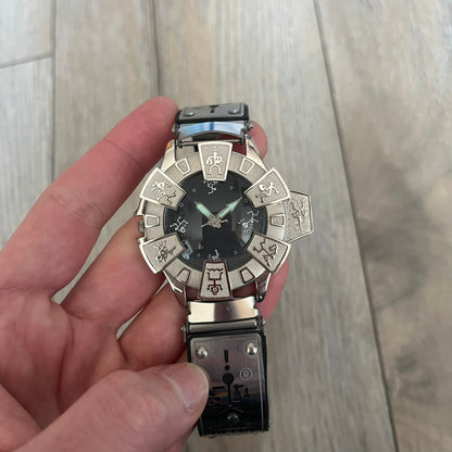 Hi-Tek Alexander “Running Man” 1990s Analog Watch is a stainless steel watch featuring a black dial and full steel case with integrated bracelet strap. The bezel includes a rotating top layer decorated with Hi-Tek character figures in various poses, while the dial replaces traditional numerals with similar character graphics. The seconds hand is designed as a character figure, and the hour and minute hands feature glow-in-the-dark functionality.