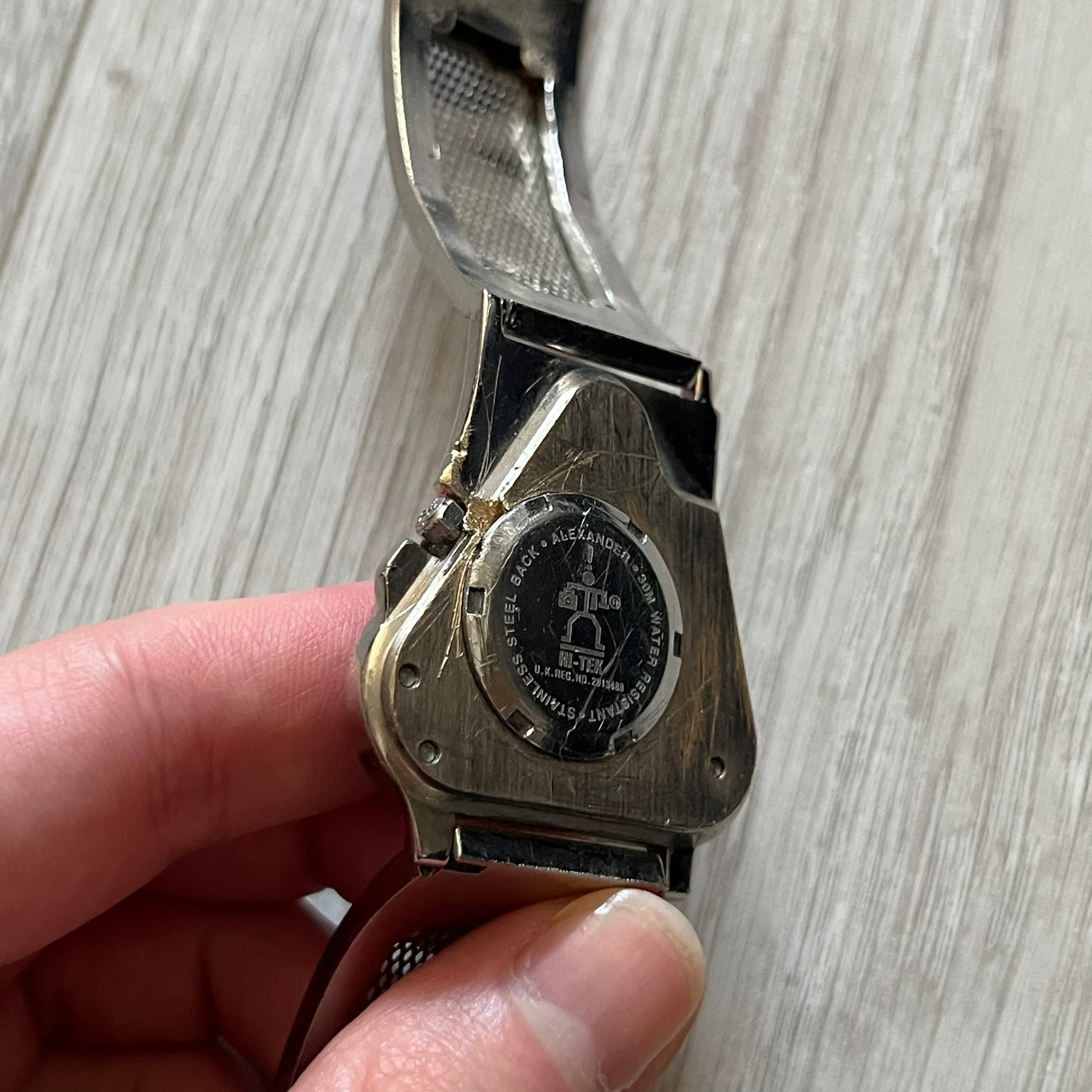 The Hi-Tek Alexander “The Engine” analog watch is a 1990s model made in England, designed with a sculptural case shaped like a motorcycle engine. It features a black dial with Alexander Hi-Tek figure logos in place of hour markers, pink hour and minute hands, and a Hi-Tek figure logo used as the seconds hand. A small sub-section at the bottom displays the day in numeric form, while visible screws and textured detailing are integrated into the engine-style face.&nbsp;The watch has an alloy case with a stainl