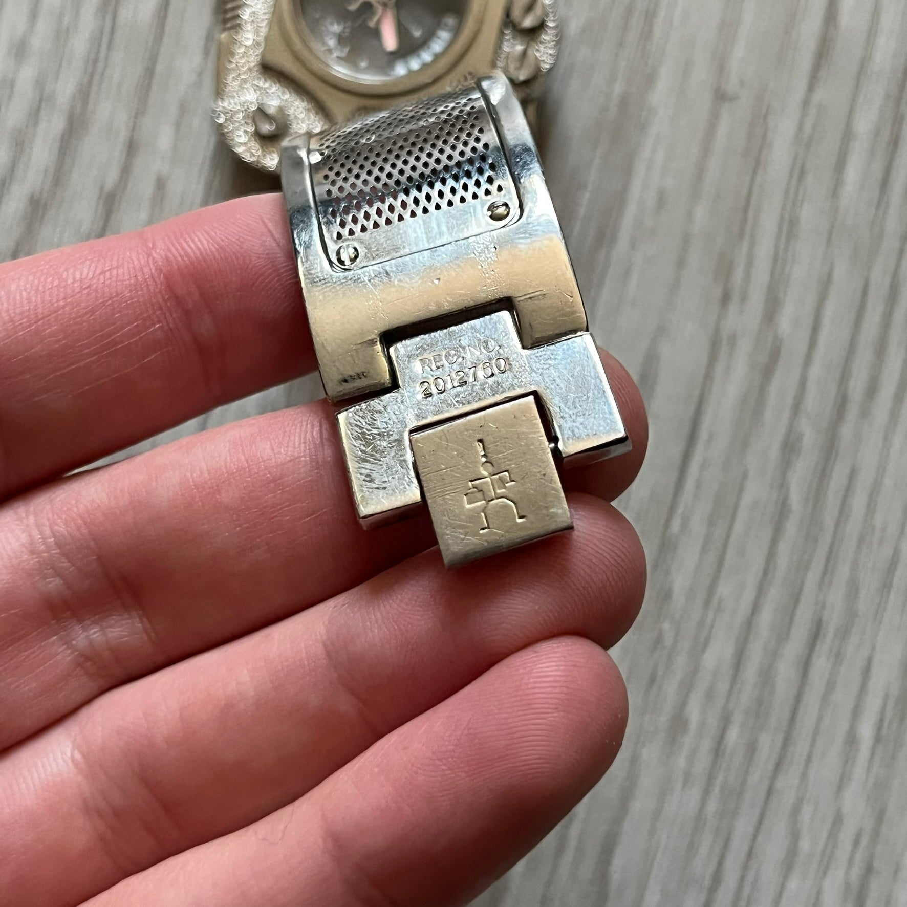 The Hi-Tek Alexander “The Engine” analog watch is a 1990s model made in England, designed with a sculptural case shaped like a motorcycle engine. It features a black dial with Alexander Hi-Tek figure logos in place of hour markers, pink hour and minute hands, and a Hi-Tek figure logo used as the seconds hand. A small sub-section at the bottom displays the day in numeric form, while visible screws and textured detailing are integrated into the engine-style face.&nbsp;The watch has an alloy case with a stainl