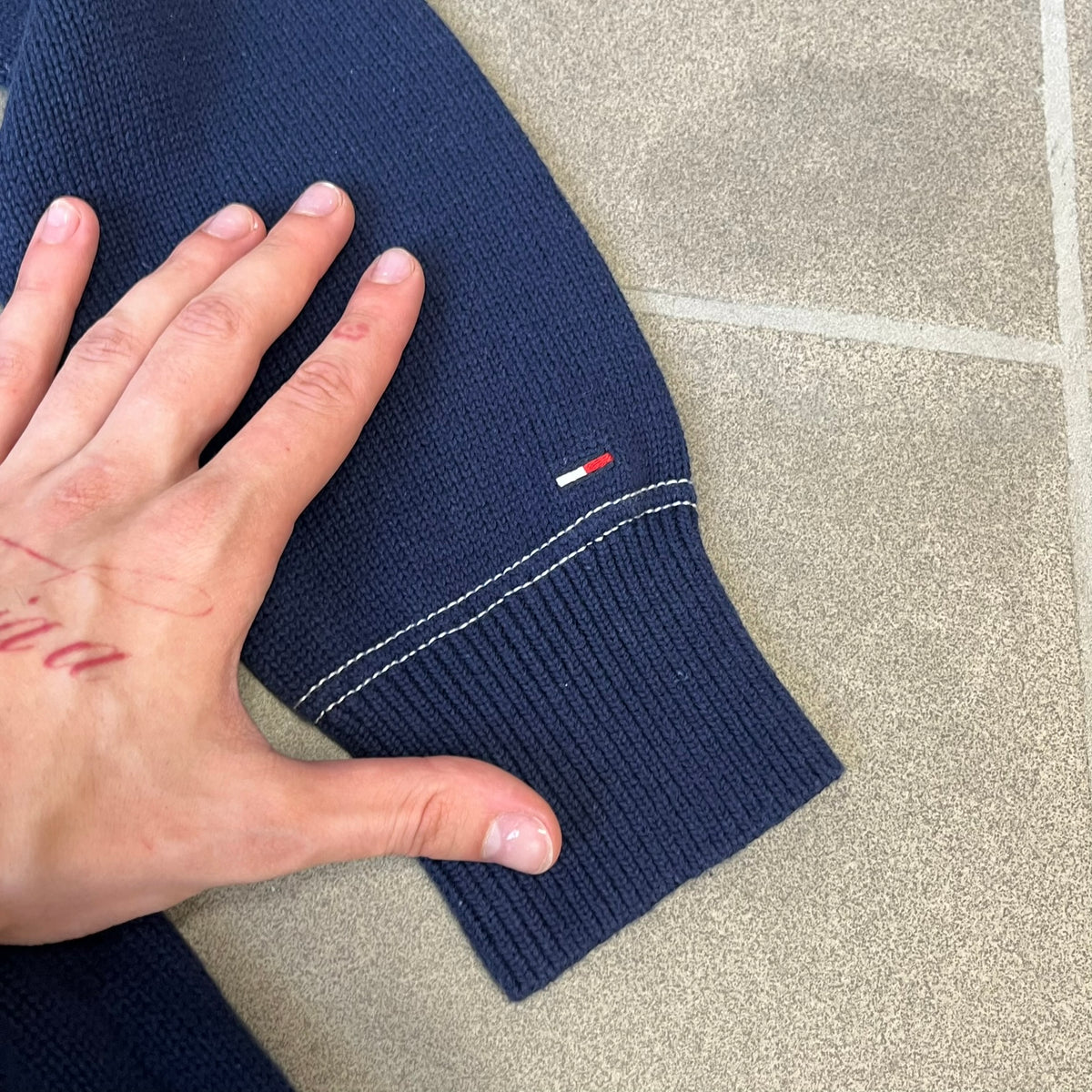 Hilfiger Denim 2012 Navy Varsity Cardigan is a navy cardigan with a white collar/hem trim and brown buttons, featuring two front pockets. It includes a large fuzzy "H" patch with text, two white straps on one sleeve, and a fuzzy white and navy "IV CHAMPS '85" patch.