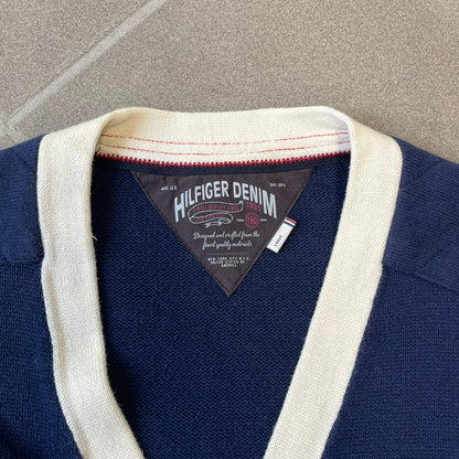 Hilfiger Denim 2012 Navy Varsity Cardigan is a navy cardigan with a white collar/hem trim and brown buttons, featuring two front pockets. It includes a large fuzzy "H" patch with text, two white straps on one sleeve, and a fuzzy white and navy "IV CHAMPS '85" patch.