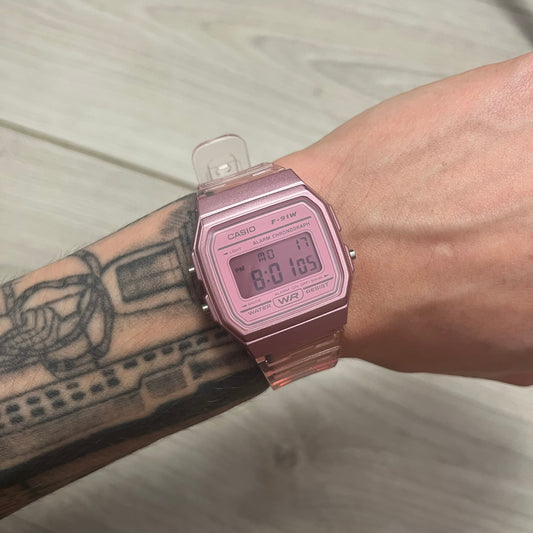 Pink digital watch on a wrist with a tattooed arm.