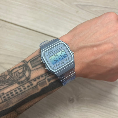 A digital Casio watch in blue color, displayed on a person's wrist against a wooden background.