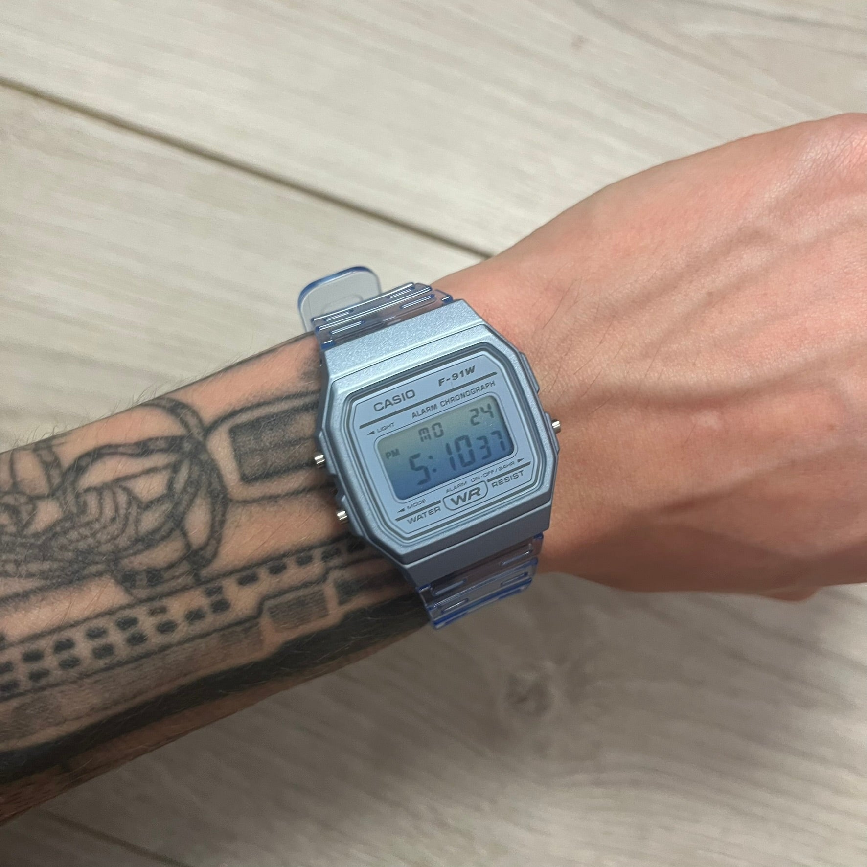 Digital watch on a wrist with a tattooed arm.