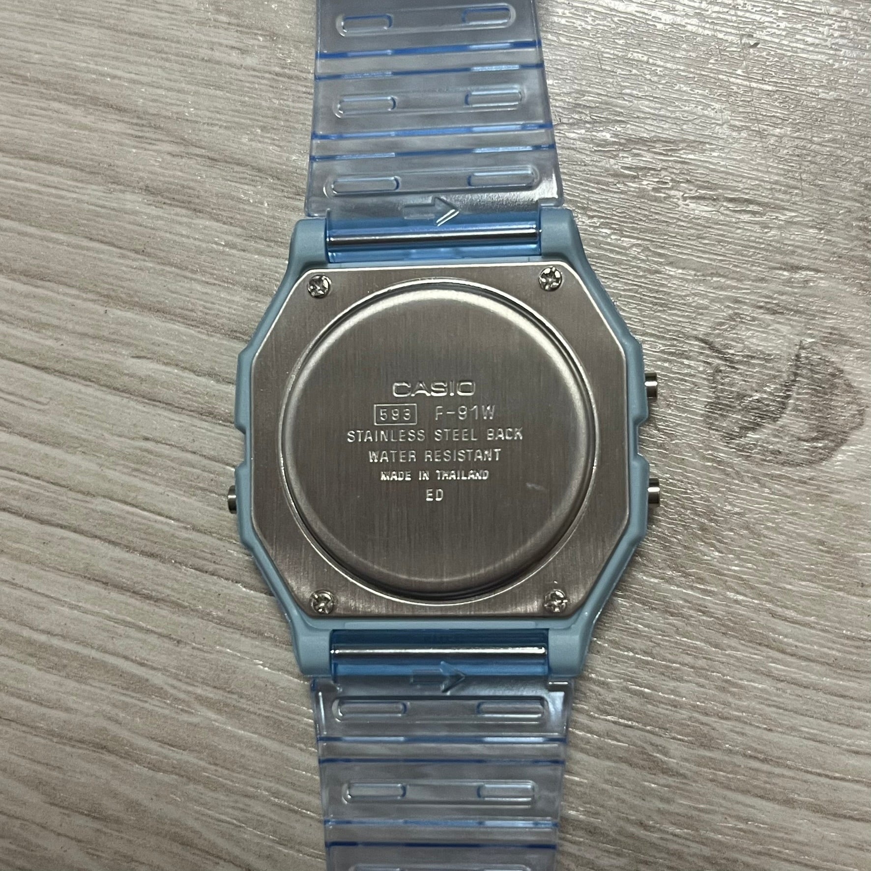 Back of a Casio watch with blue strap on wooden surface