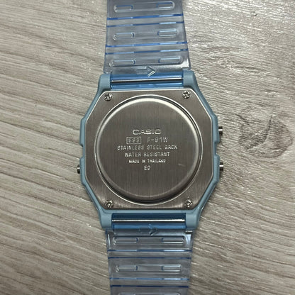 Back of a Casio watch with blue strap on wooden surface