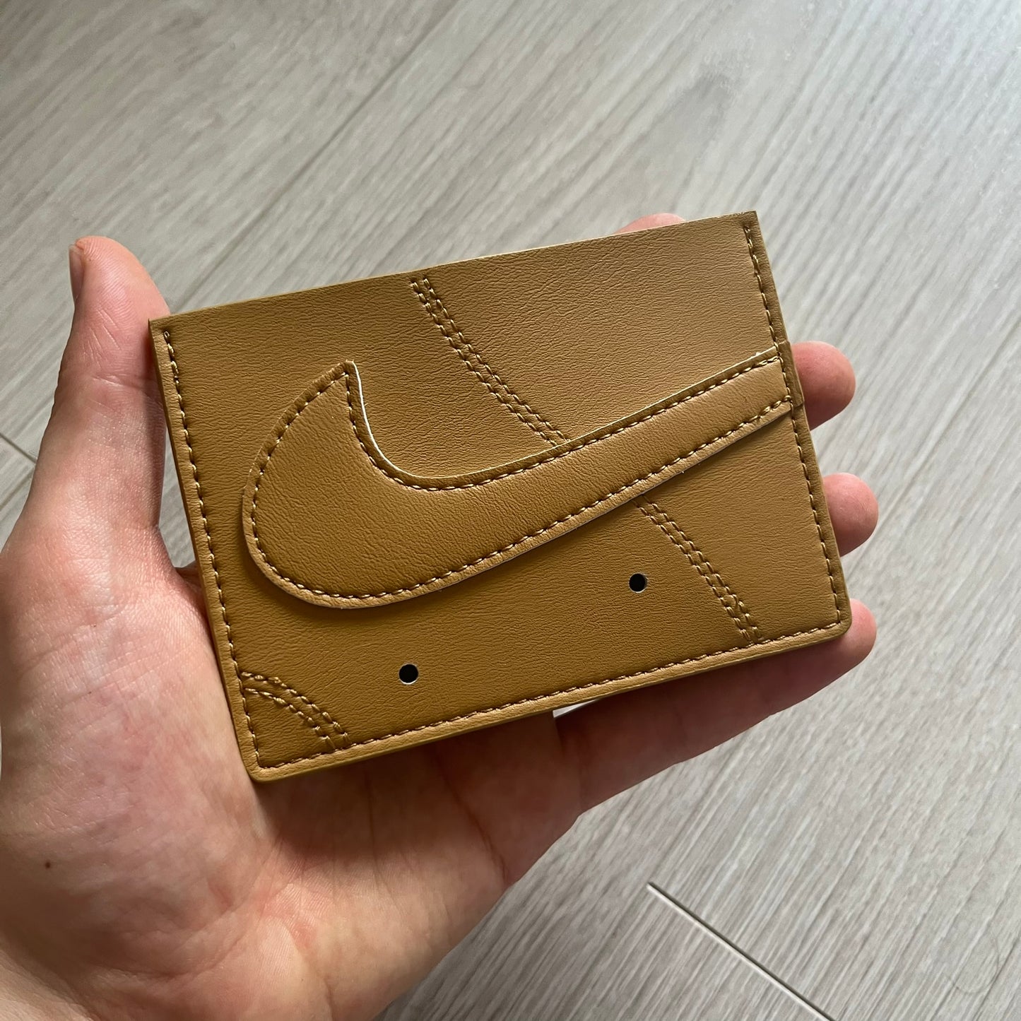 Brown leather wallet with a logo held in a hand on a wooden surface