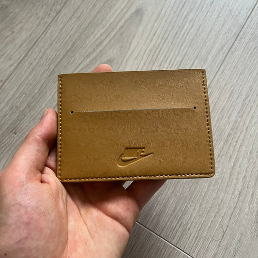 Brown leather cardholder with Nike logo held in a hand on a wooden surface