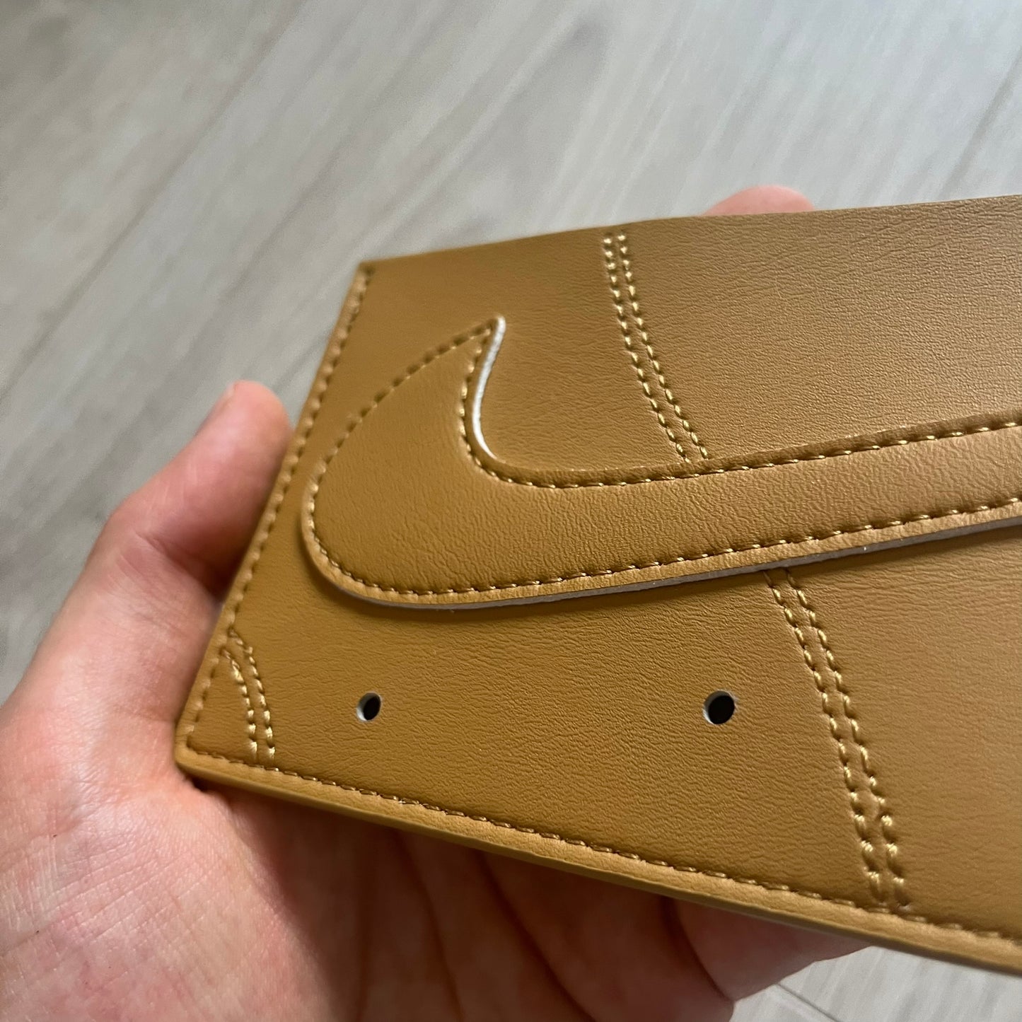 Beige leather wallet with a brand logo held in a hand on a wooden surface
