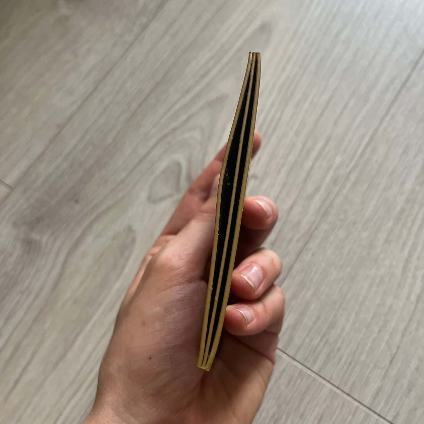 Hand holding a cylindrical object with black stripes on a wooden floor.