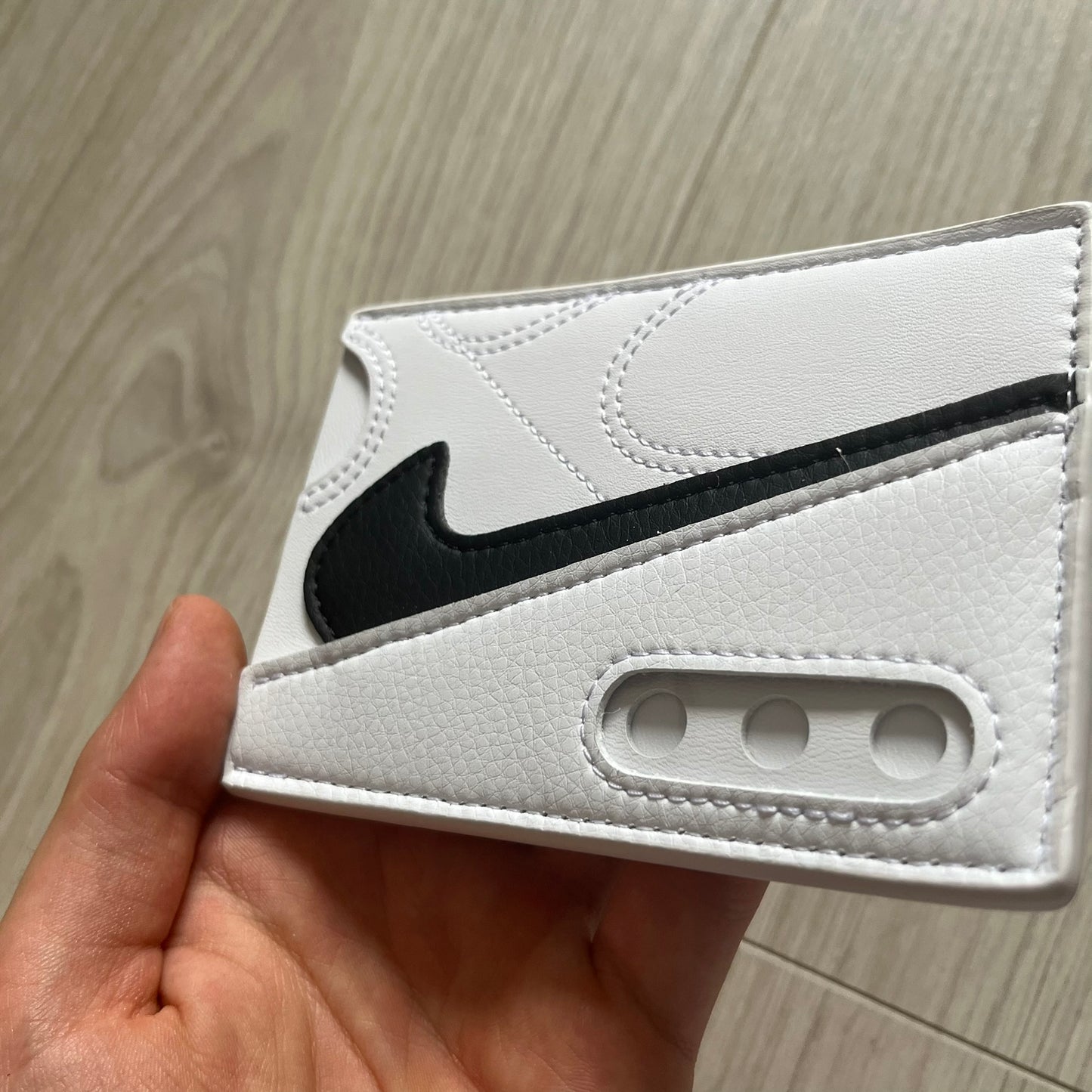 White wallet with black logo held by a hand on a wooden surface