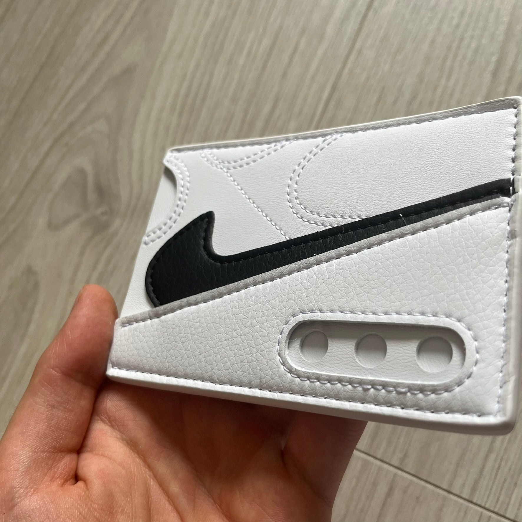 White wallet with black logo held by a hand on a wooden surface