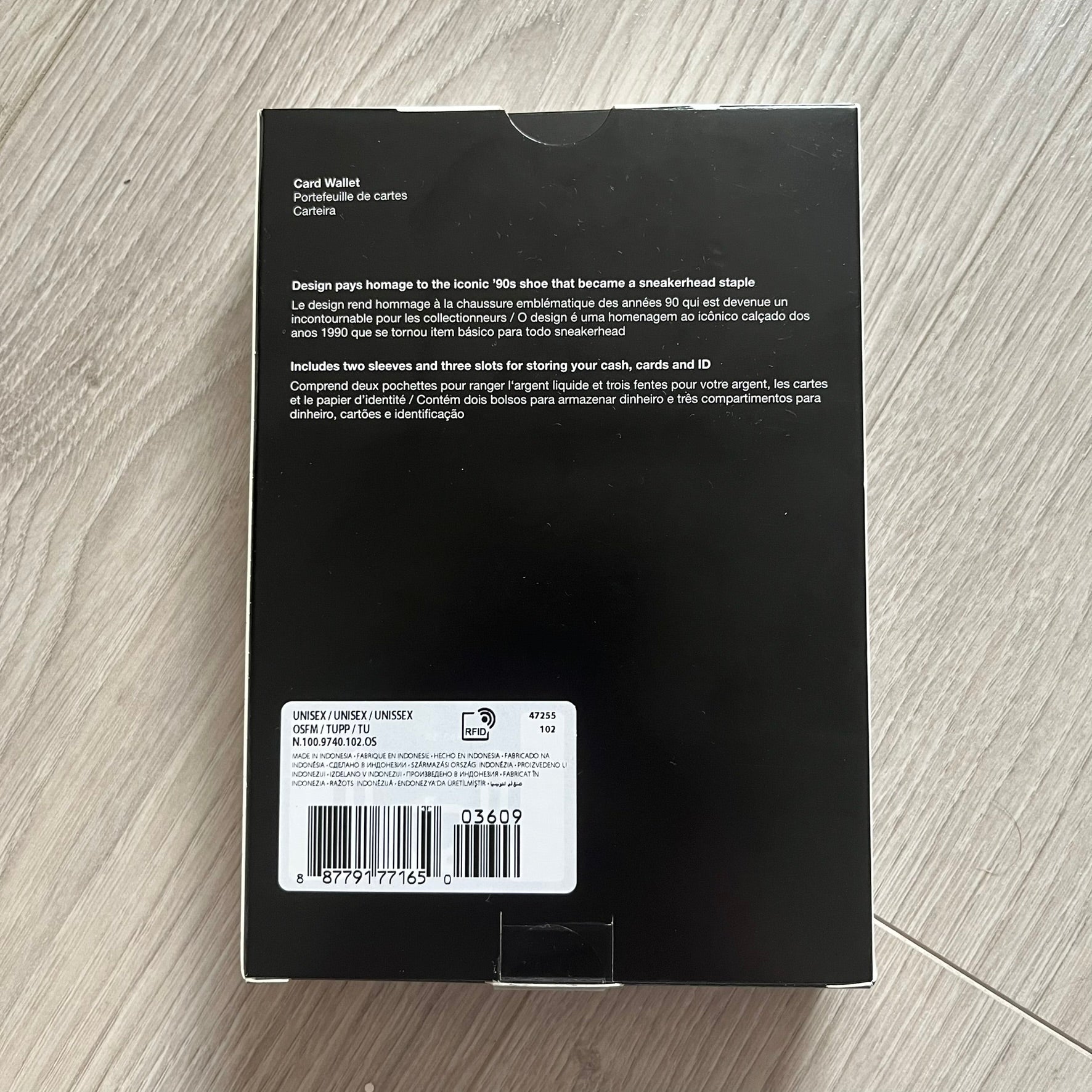Black card wallet packaging with text and barcode on a wooden surface