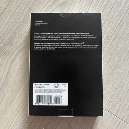 Black card wallet packaging with text and barcode on a wooden surface