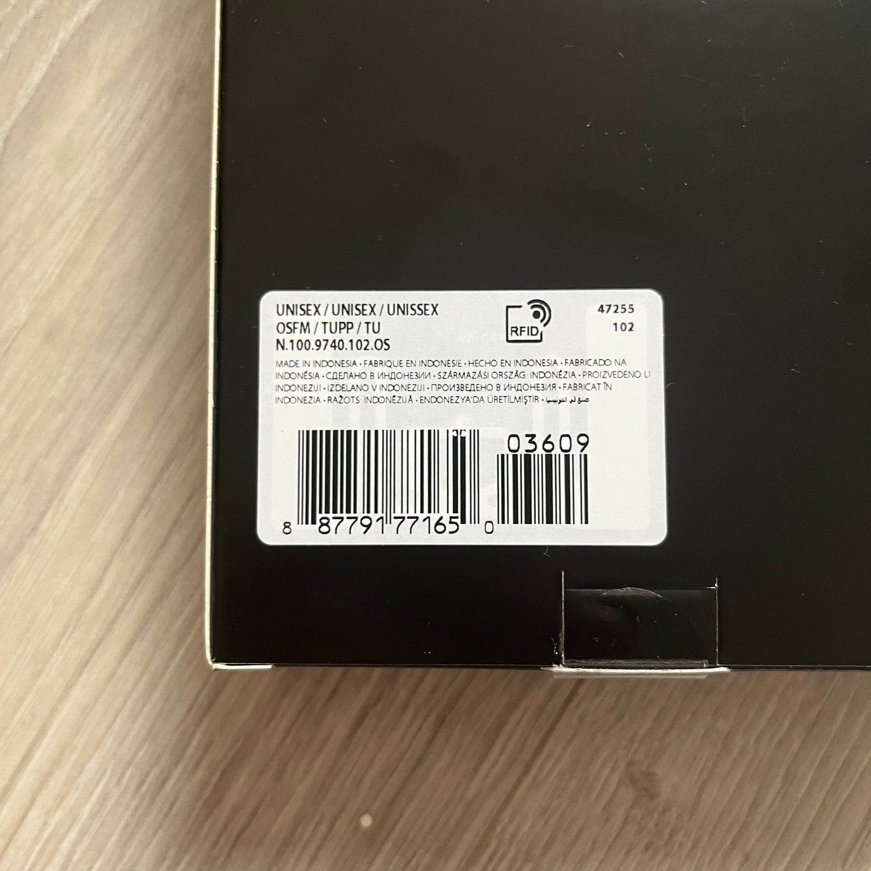 Back of a black product packaging with a label and barcode on a wooden surface
