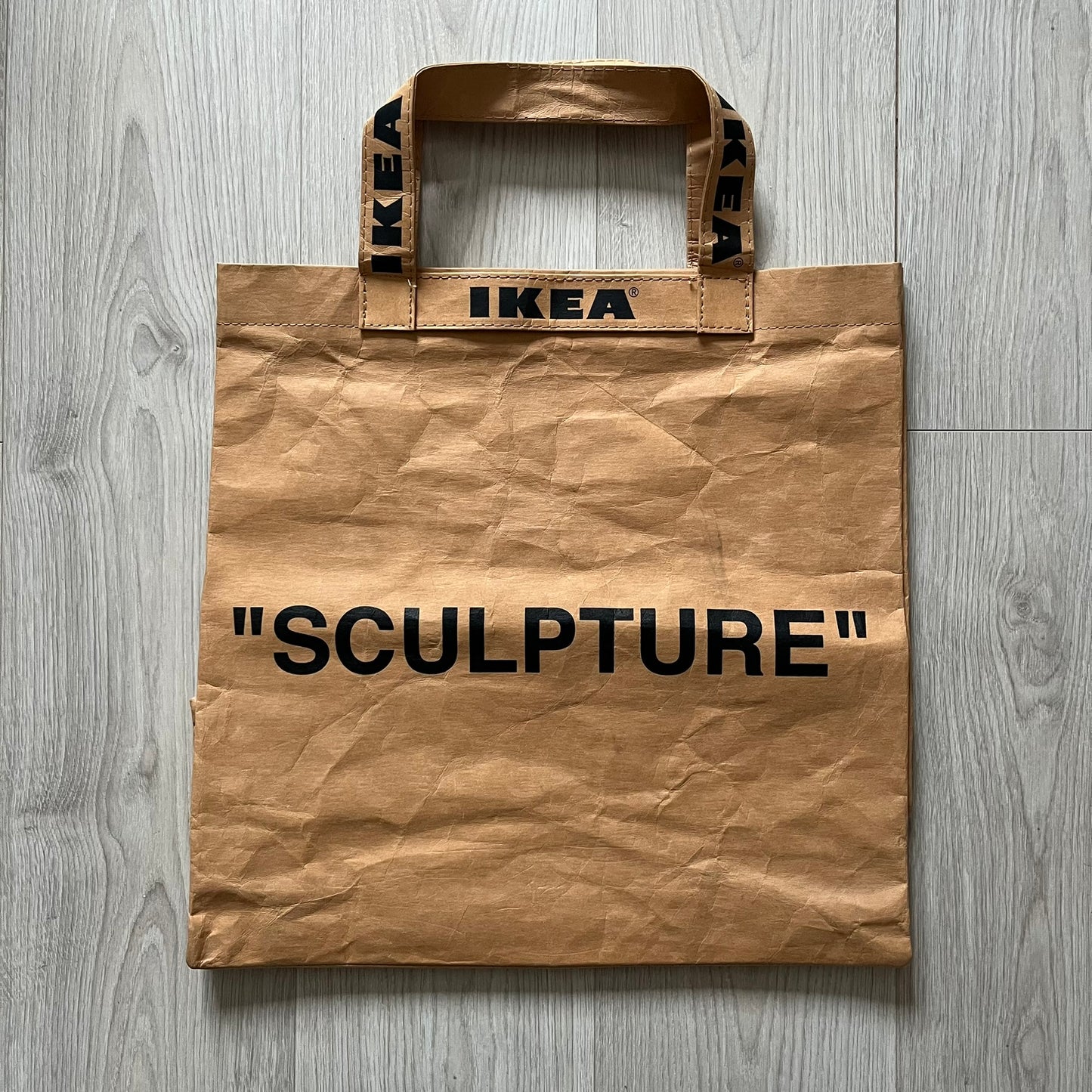 Ikea x Virgil Abloh Markerad "Sculpture" Carrier Bag from FW19 reimagines the iconic blue Frakta tote in reinforced brown paper. Embellished with Abloh’s signature quotation marks, the “SCULPTURE” print transforms a utilitarian object into conceptual design. A collectible symbol of functional art and everyday irony.