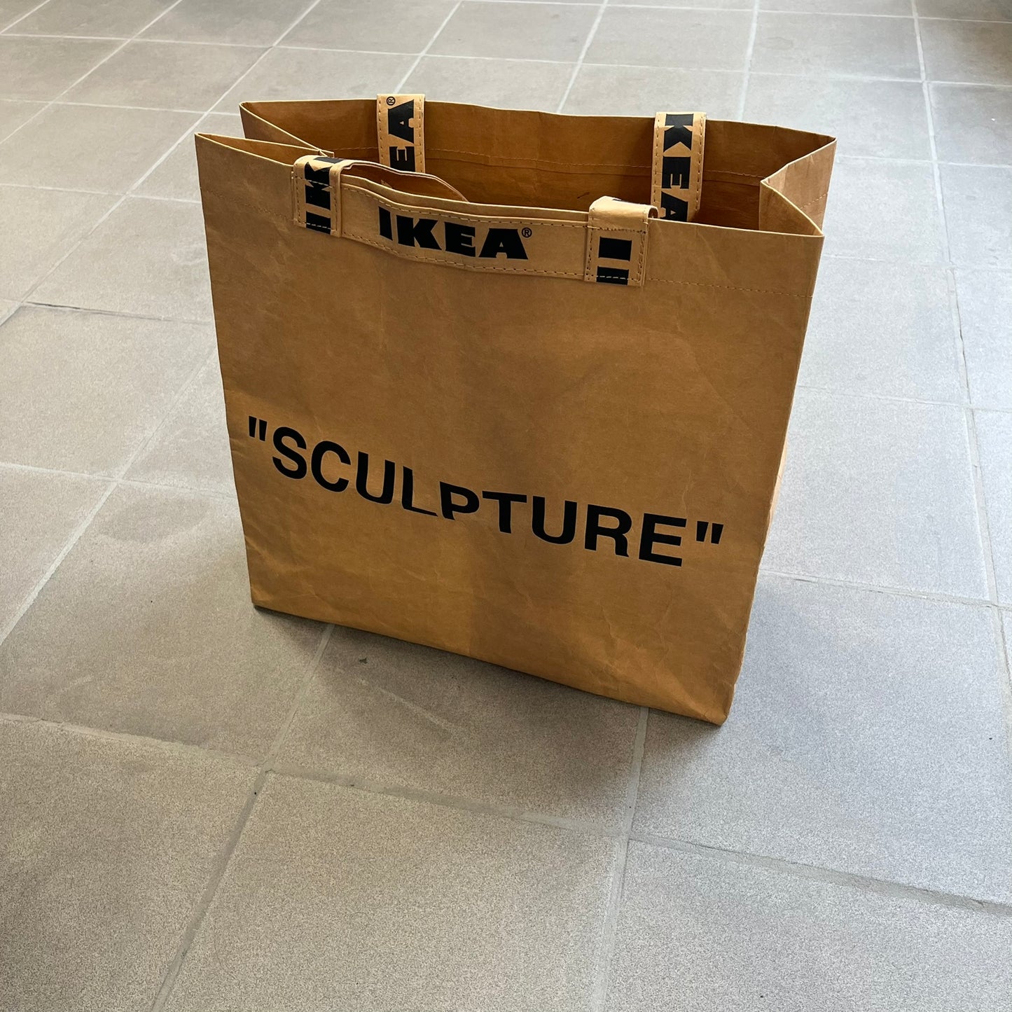 Ikea x Virgil Abloh Markerad "Sculpture" Carrier Bag from FW19 reimagines the iconic blue Frakta tote in reinforced brown paper. Embellished with Abloh’s signature quotation marks, the “SCULPTURE” print transforms a utilitarian object into conceptual design. A collectible symbol of functional art and everyday irony.
