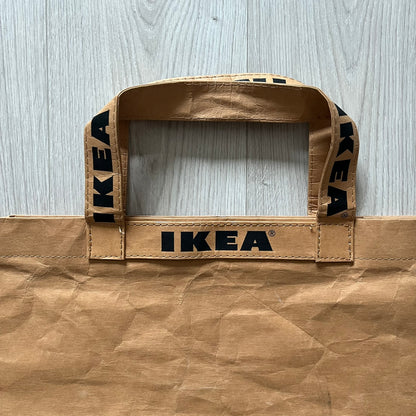 Ikea x Virgil Abloh Markerad "Sculpture" Carrier Bag from FW19 reimagines the iconic blue Frakta tote in reinforced brown paper. Embellished with Abloh’s signature quotation marks, the “SCULPTURE” print transforms a utilitarian object into conceptual design. A collectible symbol of functional art and everyday irony.