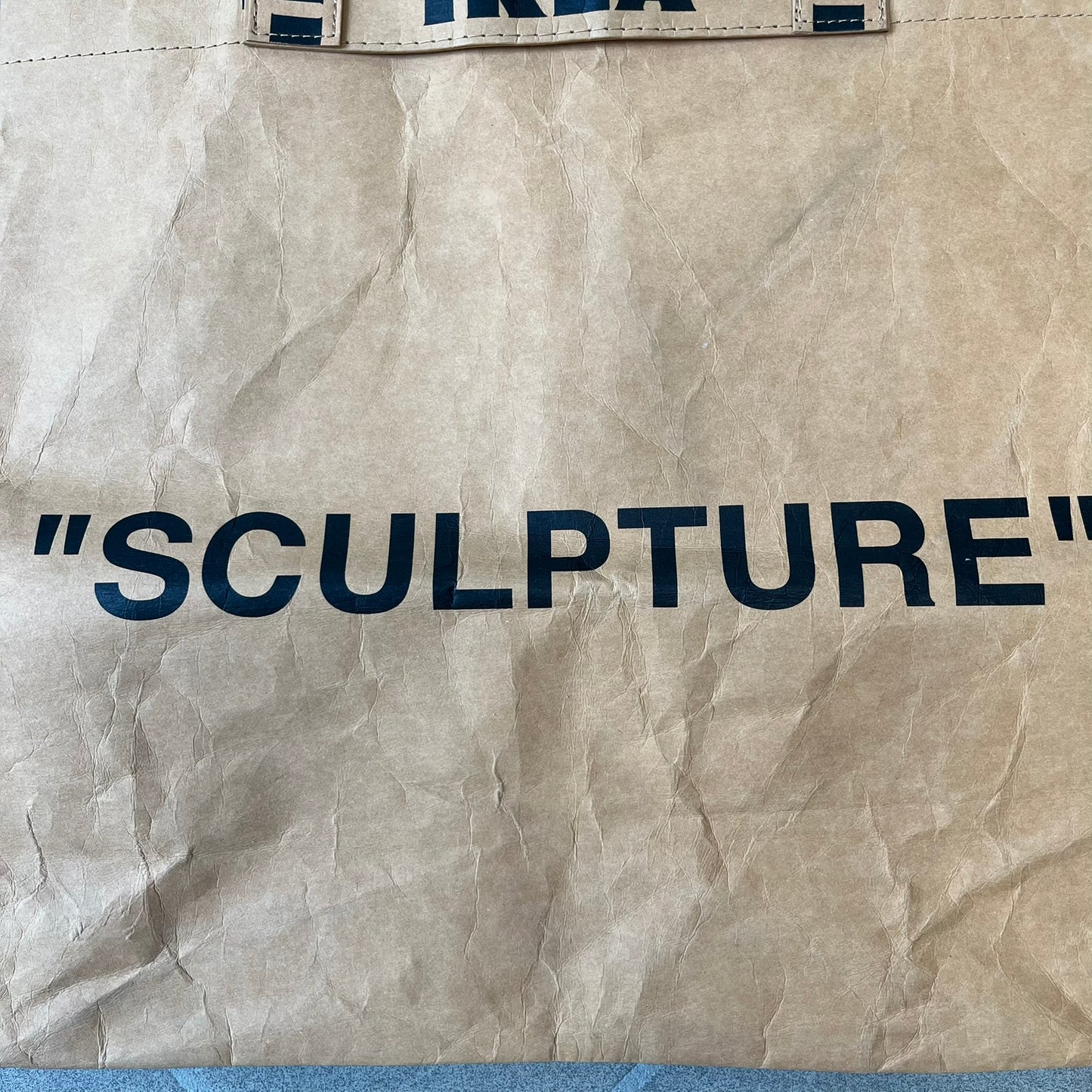 Ikea x Virgil Abloh Markerad "Sculpture" Carrier Bag from FW19 reimagines the iconic blue Frakta tote in reinforced brown paper. Embellished with Abloh’s signature quotation marks, the “SCULPTURE” print transforms a utilitarian object into conceptual design. A collectible symbol of functional art and everyday irony.