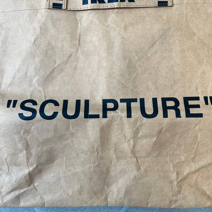 Ikea x Virgil Abloh Markerad "Sculpture" Carrier Bag from FW19 reimagines the iconic blue Frakta tote in reinforced brown paper. Embellished with Abloh’s signature quotation marks, the “SCULPTURE” print transforms a utilitarian object into conceptual design. A collectible symbol of functional art and everyday irony.