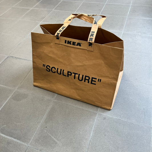 Ikea x Virgil Abloh Markerad "Sculpture" Carrier Bag from FW19 reimagines the iconic blue Frakta tote in reinforced brown paper. Embellished with Abloh’s signature quotation marks, the “SCULPTURE” print transforms a utilitarian object into conceptual design. A collectible symbol of functional art and everyday irony.