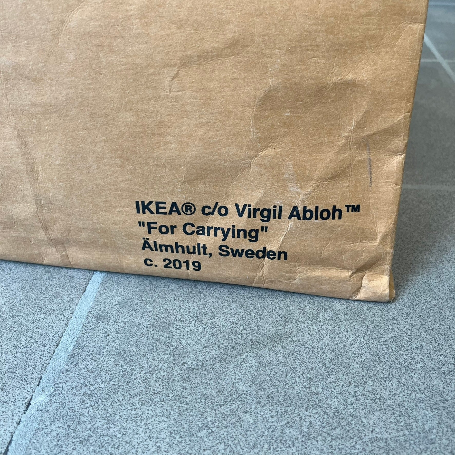 Ikea x Virgil Abloh Markerad "Sculpture" Carrier Bag from FW19 reimagines the iconic blue Frakta tote in reinforced brown paper. Embellished with Abloh’s signature quotation marks, the “SCULPTURE” print transforms a utilitarian object into conceptual design. A collectible symbol of functional art and everyday irony.