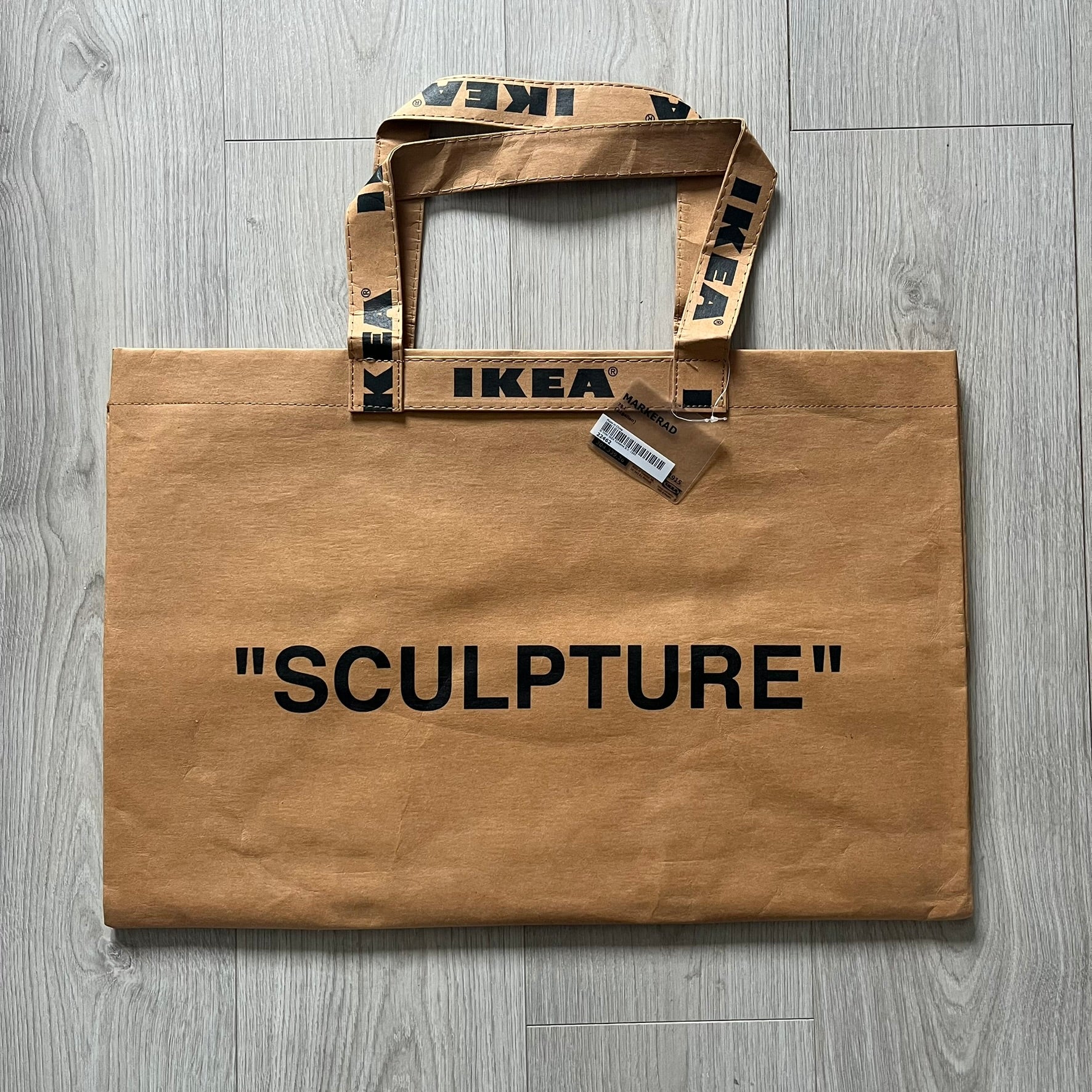 Ikea x Virgil Abloh Markerad "Sculpture" Carrier Bag from FW19 reimagines the iconic blue Frakta tote in reinforced brown paper. Embellished with Abloh’s signature quotation marks, the “SCULPTURE” print transforms a utilitarian object into conceptual design. A collectible symbol of functional art and everyday irony.