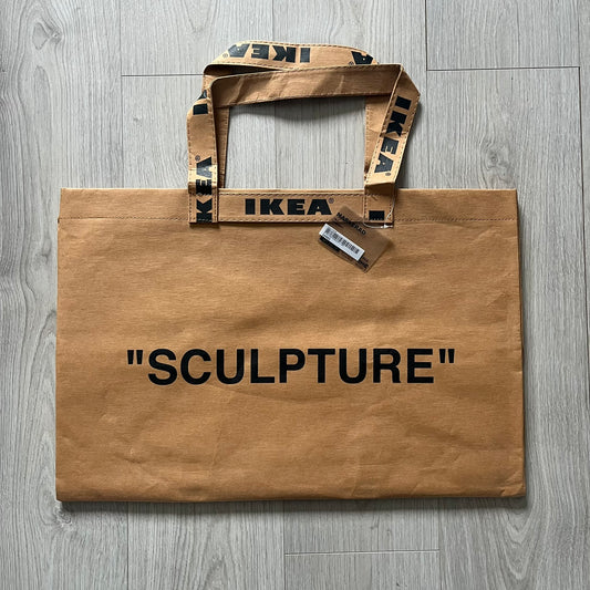 Ikea x Virgil Abloh Markerad "Sculpture" Carrier Bag from FW19 reimagines the iconic blue Frakta tote in reinforced brown paper. Embellished with Abloh’s signature quotation marks, the “SCULPTURE” print transforms a utilitarian object into conceptual design. A collectible symbol of functional art and everyday irony.
