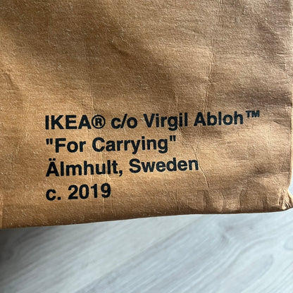 Ikea x Virgil Abloh Markerad "Sculpture" Carrier Bag from FW19 reimagines the iconic blue Frakta tote in reinforced brown paper. Embellished with Abloh’s signature quotation marks, the “SCULPTURE” print transforms a utilitarian object into conceptual design. A collectible symbol of functional art and everyday irony.