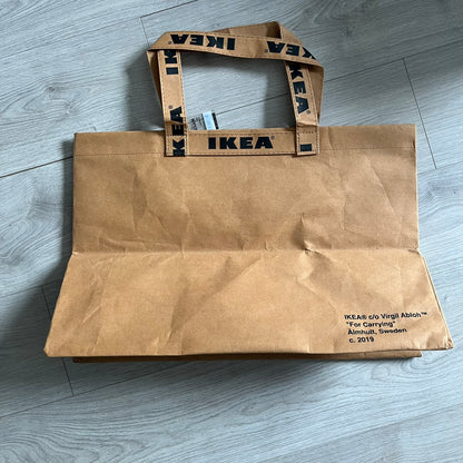 Ikea x Virgil Abloh Markerad "Sculpture" Carrier Bag from FW19 reimagines the iconic blue Frakta tote in reinforced brown paper. Embellished with Abloh’s signature quotation marks, the “SCULPTURE” print transforms a utilitarian object into conceptual design. A collectible symbol of functional art and everyday irony.