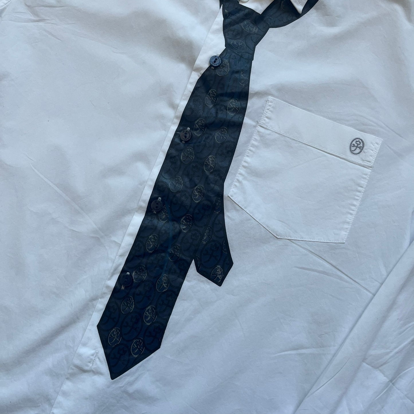 JC De Castelbajac AW08 Loose Tie Shirt is a white long-sleeve shirt from the Autumn/Winter 2008 collection, made in Italy from 100% cotton. The design features a printed navy tie with JC monogram on the front, a chest pocket with small logo embroidery, and additional logo embroidery on the back below the collar and on the sleeve. It includes mother-of-pearl buttons with contrasting white and navy detailing, matching the printed tie graphic.