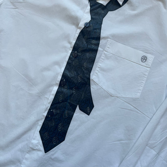 JC De Castelbajac AW08 Loose Tie Shirt is a white long-sleeve shirt from the Autumn/Winter 2008 collection, made in Italy from 100% cotton. The design features a printed navy tie with JC monogram on the front, a chest pocket with small logo embroidery, and additional logo embroidery on the back below the collar and on the sleeve. It includes mother-of-pearl buttons with contrasting white and navy detailing, matching the printed tie graphic.