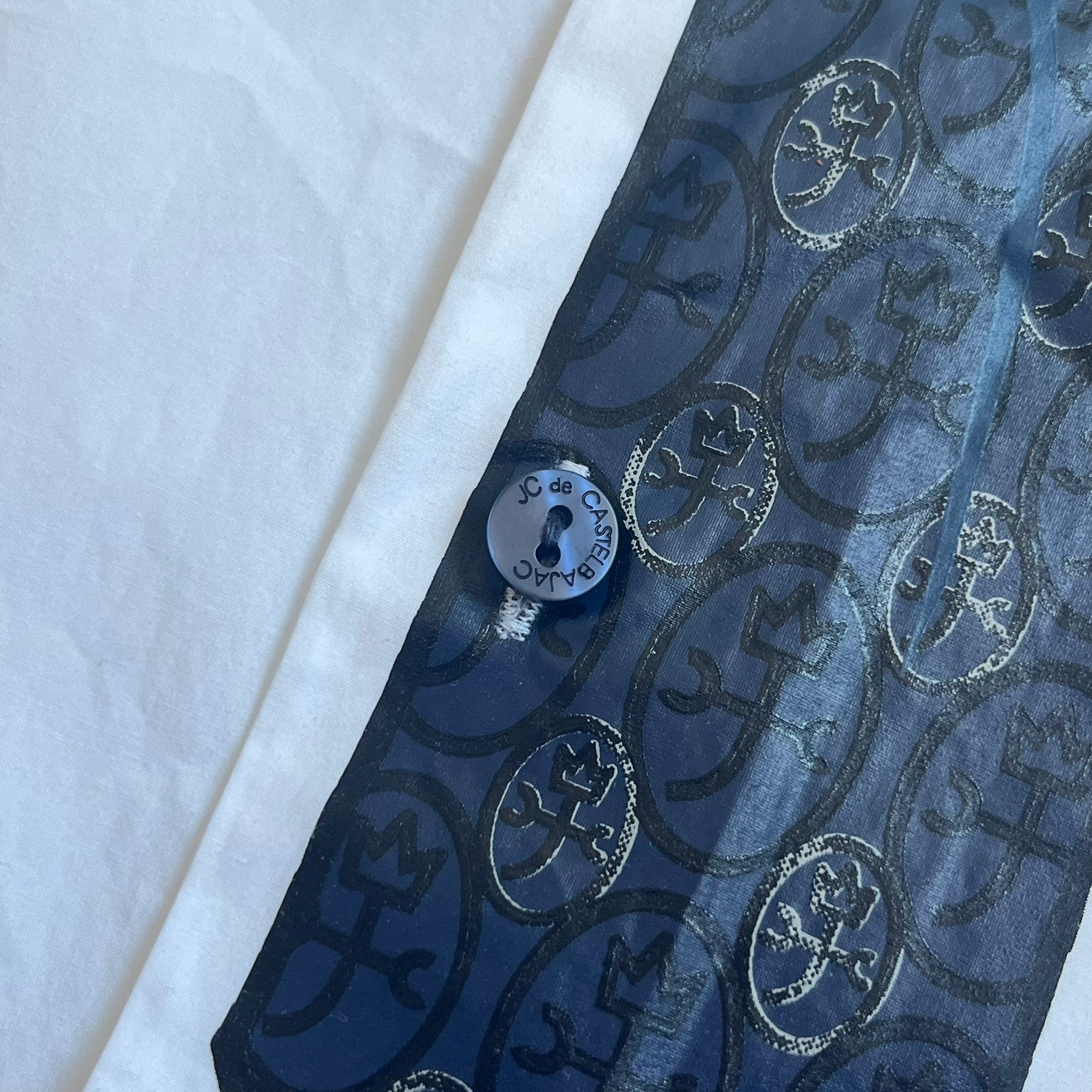 JC De Castelbajac AW08 Loose Tie Shirt is a white long-sleeve shirt from the Autumn/Winter 2008 collection, made in Italy from 100% cotton. The design features a printed navy tie with JC monogram on the front, a chest pocket with small logo embroidery, and additional logo embroidery on the back below the collar and on the sleeve. It includes mother-of-pearl buttons with contrasting white and navy detailing, matching the printed tie graphic.