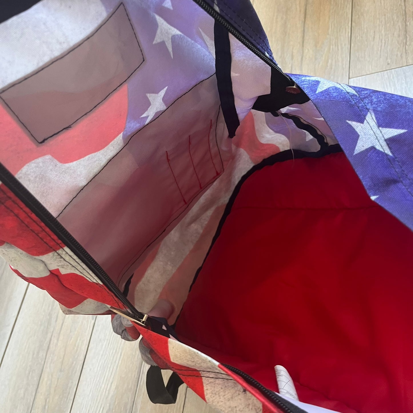 JanSport High Stakes Multi Grunge USA Backpack (JS00TRS70GM) is a backpack featuring an all-over distressed American flag design across the front and side panels. The flag graphic has a deliberately worn and faded appearance, giving it a vintage grunge look. The back panel and shoulder straps are finished in black, while the front includes the classic JanSport logo patch.