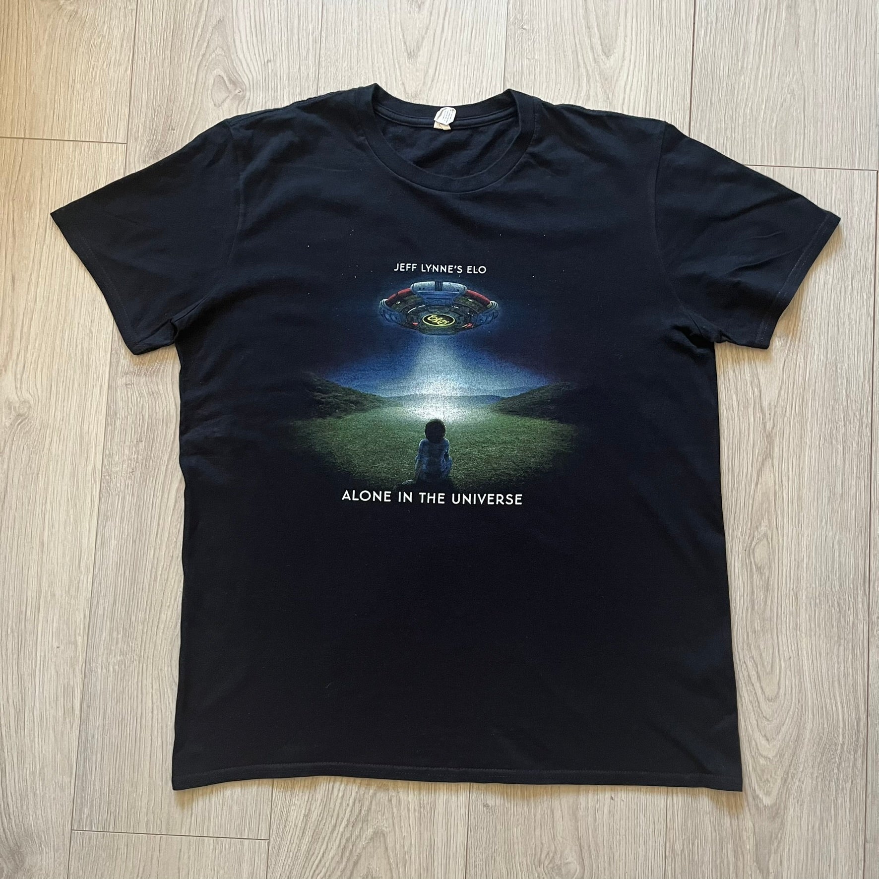Official tour tee from Jeff Lynne’s Alone in the Universe era, released in 2015. The shirt comes in black with the album artwork printed on the front, while the back lists the 2015/2016 tour stops including London, Amsterdam, and Oberhausen