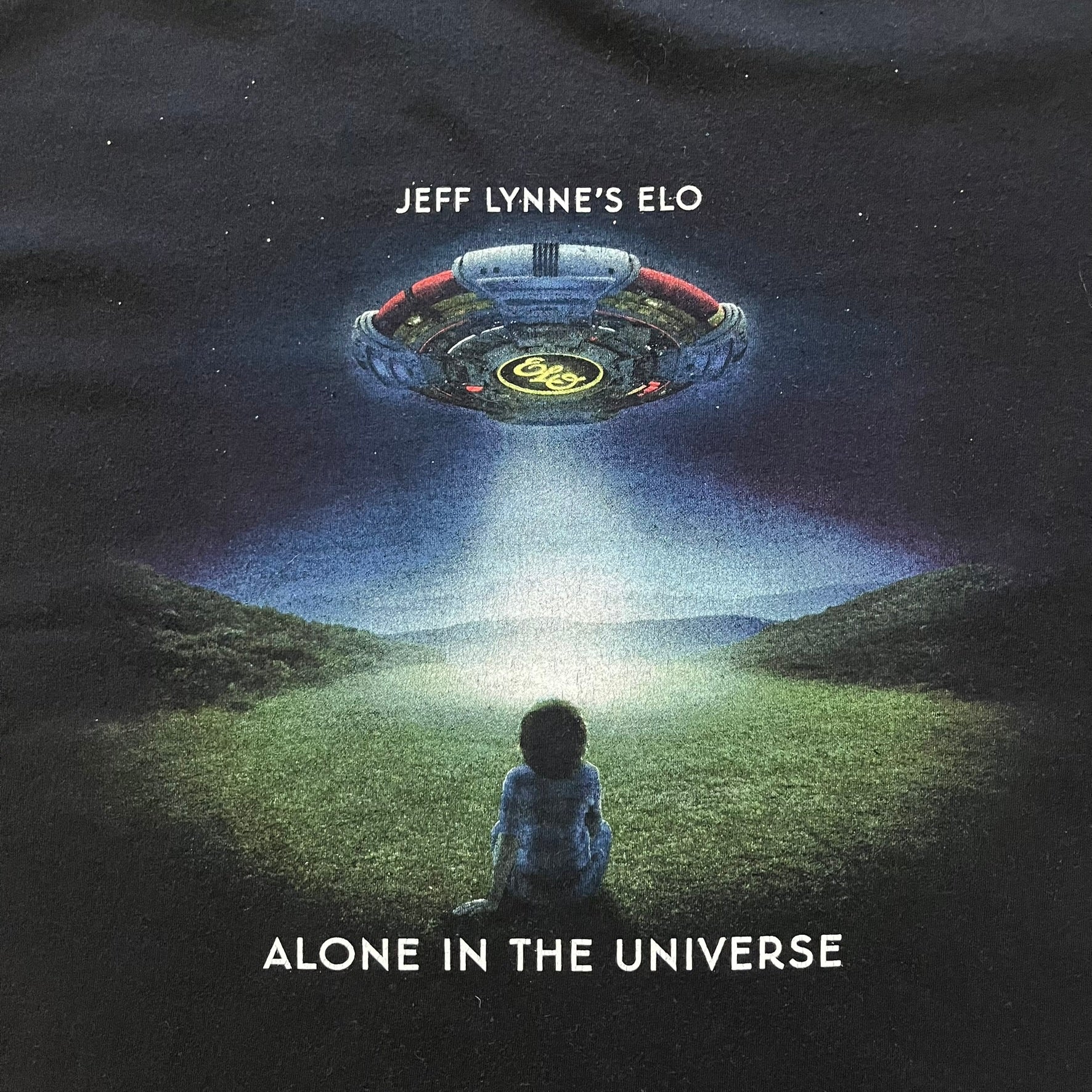 Official tour tee from Jeff Lynne’s Alone in the Universe era, released in 2015. The shirt comes in black with the album artwork printed on the front, while the back lists the 2015/2016 tour stops including London, Amsterdam, and Oberhausen