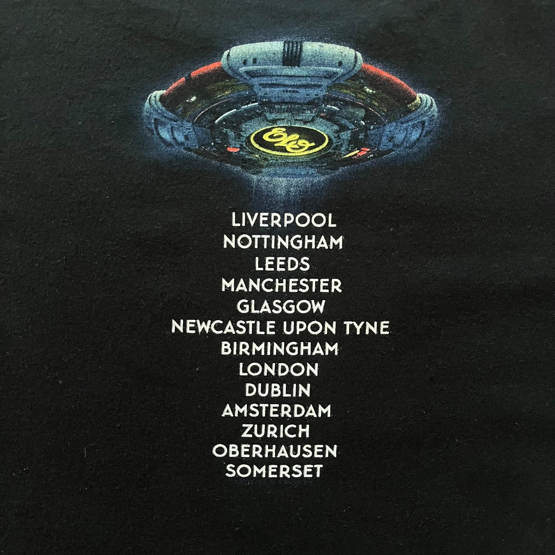 Official tour tee from Jeff Lynne’s Alone in the Universe era, released in 2015. The shirt comes in black with the album artwork printed on the front, while the back lists the 2015/2016 tour stops including London, Amsterdam, and Oberhausen